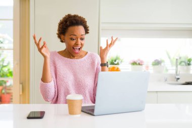 Çılgın kutlama bilgisayar dizüstü kullanarak çalışma ve silah ile başarı için heyecanlı çığlık kaldırdı ve açık gözleri hayret genç Afro-Amerikan kadın. Kazanan kavramı