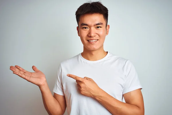 年轻的亚洲中国男子穿着T恤站在孤立的白色背景惊讶和微笑的相机 同时呈现与手和手指 — 图库照片