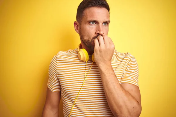 年轻的帅哥戴着耳机听音乐 在黄色孤立的背景上显得紧张和紧张 双手咬着指甲 焦虑问题 — 图库照片
