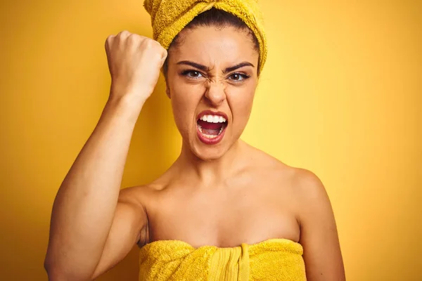 Young beautiful woman wearing towel after shower over isolated yellow background annoyed and frustrated shouting with anger, crazy and yelling with raised hand, anger concept