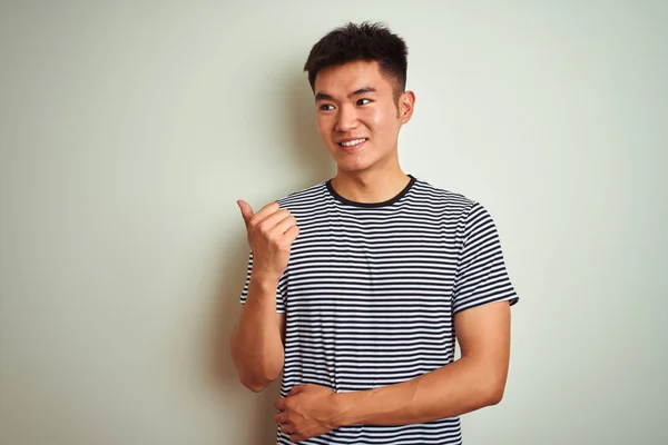 孤立した白い背景の上に立つストライプのTシャツを着た若いアジア人の男性は 幸せそうな顔で微笑み 親指を上げて横を向いている — ストック写真