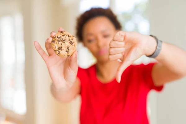 年轻的非洲裔美国妇女吃巧克力饼干与愤怒的脸 负面的迹象显示不喜欢与拇指向下 拒绝概念 — 图库照片