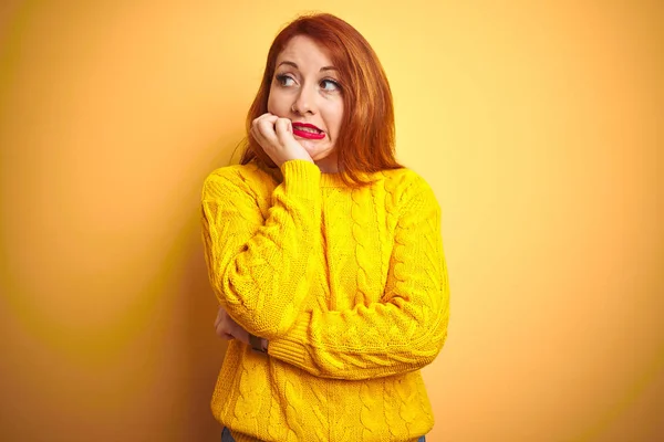 美丽的红头发女人穿着冬季毛衣站在孤立的黄色背景上 看起来很紧张 双手放在咬指甲的嘴上 焦虑问题 — 图库照片
