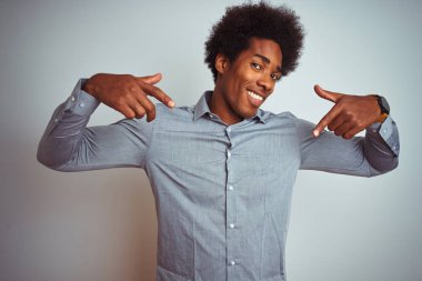 Izole beyaz arka plan üzerinde gri gömlek giyen afro saçlı genç afro-amerikan adam yüzünde gülümseme ile emin görünümlü, parmakları gururlu ve mutlu kendini işaret.