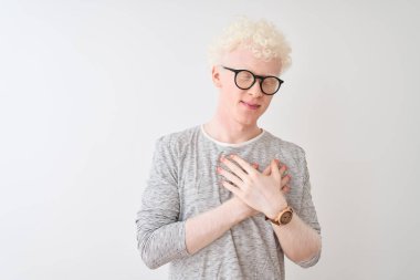 Genç albino sarışın adam çizgili tişört ve gözlük takıyor izole edilmiş beyaz arka plan üzerine gülümsüyor elleri göğsünde kapalı ve yüzünde minnet ifadesi var. Sağlık kavramı.