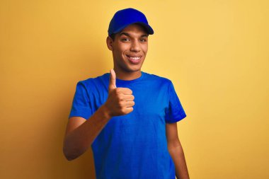 Sarı arka planda duran yakışıklı Arap teslimatçı mutlu bir el hareketi yapıyor. Kameraya bakıp başarıyı gösteren ifade onaylanıyor.