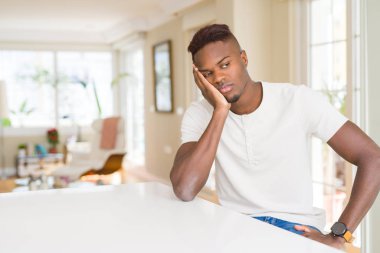 Yakışıklı afro-amerikan adam evde beyaz masada yorgun görünümlü ve çapraz kolları ile depresyon sorunları ile sıkılmış düşünme.