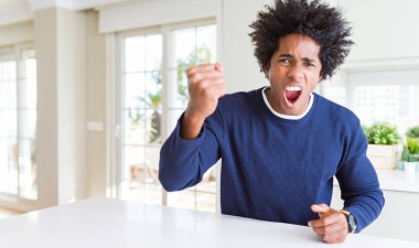 Genç afro-amerikan adam evde oturan rahat kazak giyen kızgın ve deli yükselterek yumruk sinirli ve öfkeli öfke ile bağırırken. Öfke ve agresif kavram.