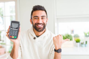 Yakışıklı İspanyol adam satış noktasını tutuyor. Terminal veri bankasını işaret ediyor ve gülümseyen bir gülümsemeyle baş parmağıyla gösteriyor.