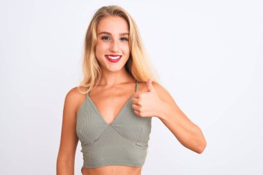 Genç güzel kadın rahat yeşil t-shirt izole beyaz arka plan üzerinde el ile jest kadar mutlu başparmak yapıyor ayakta giyiyor. Başarı gösteren kameraya bakarak ifadeyi onaylama.