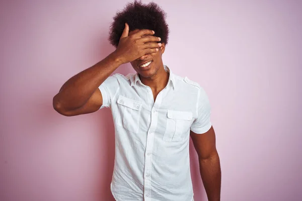 年轻的美国男子 一个头发 穿着白色衬衫站在孤立的粉红色背景微笑和笑与手在脸上覆盖眼睛惊喜 盲概念 — 图库照片