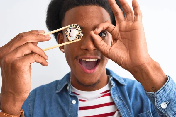 年轻的非洲裔美国男子吃寿司用筷子在孤立的白色背景与快乐的脸微笑做确定的标志手在眼睛通过手指看 — 图库照片
