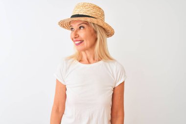 Orta yaş kadın rahat t-shirt ve şapka giyerek izole beyaz arka plan üzerinde duran yüzünde gülümseme, doğal ifade ile yan bakıyor. Gülmekten emin.