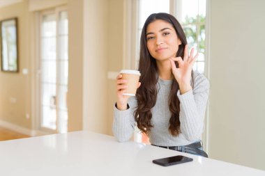 Evde kahve içen genç bir kadın parmaklarıyla imza atıyor, mükemmel bir sembol.