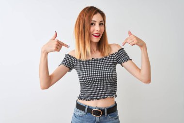 Izole beyaz arka plan üzerinde duran rahat t-shirt giyen güzel kızıl saçlı kadın yüzünde gülümseme ile emin görünümlü, parmakları gururlu ve mutlu kendini işaret.