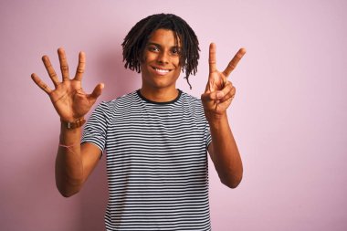Dreadlocks lacivert çizgili t-shirt giyen afro adam izole pembe arka plan üzerinde duran gösteren ve emin ve mutlu gülümserken parmakları sayısı yedi ile işaret.