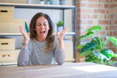 Orta yaş kıdemli kadın evde masada oturan deli ve silah ile başarı için çılgın kutluyor ve kapalı gözleri heyecanlı çığlık kaldırdı. Kazanan kavramı