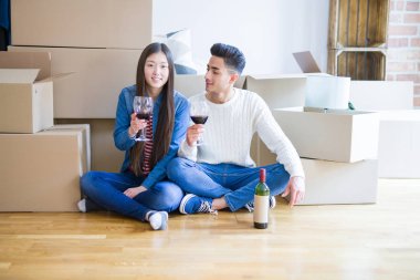 Yeni dairenin katında oturan genç Asyalı Çift, yeni bir eve taşınmak için heyecanlı bir bardak şarap içmeye gülümsüyor, karton kutular civarı
