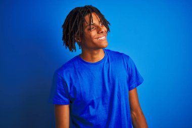 Afro amerikan adam dreadlocks t-shirt giyen izole mavi arka plan üzerinde yüz, doğal ifade gülümseme ile yan bakıyor. Gülmekten emin.