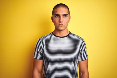 Sarı izole edilmiş arka plan şüphecisi ve gergin, sorun yüzünden somurtkan, çizgili tişört giyen genç yakışıklı adam. Negatif kişi.
