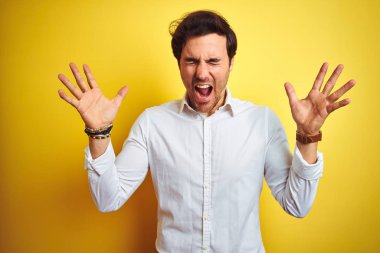 Genç yakışıklı işadamı izole sarı arka plan üzerinde duran zarif gömlek giyen kollarını kaldırdı ve kapalı gözleri heyecan çığlık ile başarı için deli ve deli kutluyor. Kazanan kavramı