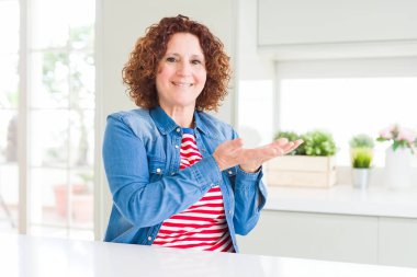 Orta yaşlı, kıvırcık saçlı, kot ceketli, elleri açık, elinde fotokopi alanı gösteren, mutlu bir gülümseme reklamı sunan orta yaşlı bir kadın.