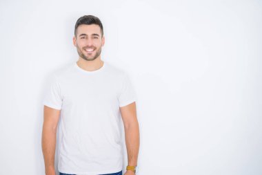 Beyaz izole arka plan üzerinde rahat beyaz t-shirt giyen mutlu gülümseyen genç yakışıklı adam