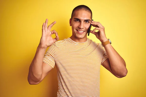 年轻英俊的男子用智能手机在黄色孤立的背景上说话 手拿着手签 很好的符号 — 图库照片