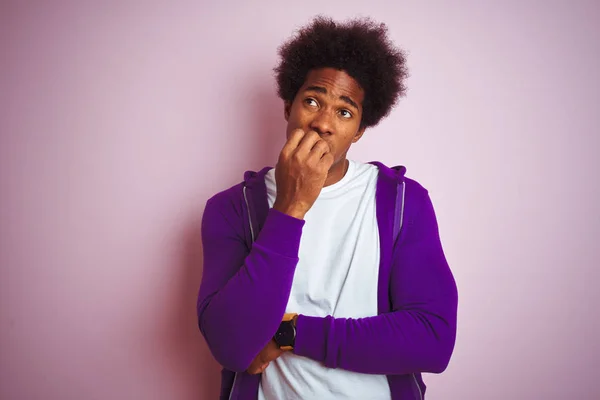 年轻的非洲裔美国男子穿着紫色运动衫站在孤立的粉红色背景上 看着紧张和紧张与嘴咬指甲的手 焦虑问题 — 图库照片