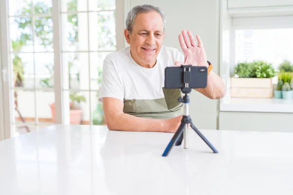 Handsome senior man waving hello to the smartphone camera doing