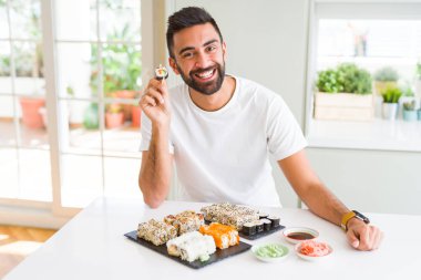 Yakışıklı adam Chopsticks kullanarak taze renkli Asya Suşi yeme mutlu gülümsüyor