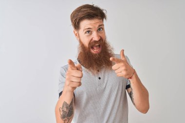 Genç kızıl İrlandalı adam izole beyaz arka plan üzerinde duran gri polo giyen mutlu ve komik yüzü ile kameraya parmakları işaret. İyi enerji ve titreşimler.