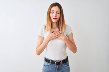 Güzel kızıl saçlı kadın kapalı gözleri ve yüzünde minnettar jest ile göğüs üzerinde gülümseyerek izole beyaz arka plan üzerinde duran rahat t-shirt giyiyor. Sağlık kavramı.