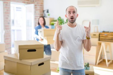 Genç çift yuvarlak karton kutular yeni bir eve hareket, evde duran kel adam şaşırmış ve şaşırmış yukarı bakarak ve parmakları ile işaret ve kolları kaldırdı.