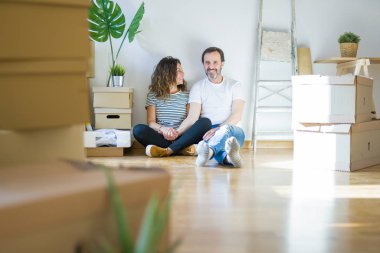 Orta yaş üst düzey romantik çift etrafında karton kutular ile daire katında oturan ve yeni bir eve taşınmak için mutlu gülümseyen aşk