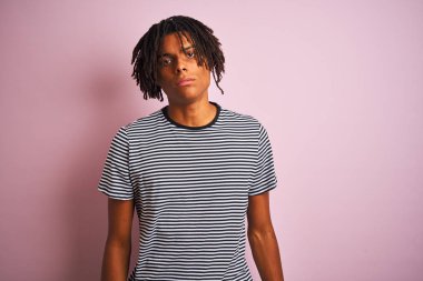 Afro man with dreadlocks wearing navy striped t-shirt standing over isolated pink background Relaxed with serious expression on face. Simple and natural looking at the camera.