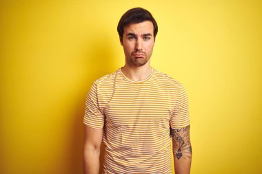 Dövme ile genç yakışıklı adam izole sarı arka plan üzerinde çizgili t-shirt giyen depresif ve sıkıntı için endişe, kızgın ve korkmuş ağlıyor. Hüzünlü ifade.