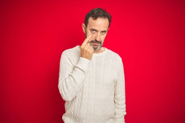 İzole kırmızı arka plan üzerinde gri saçlı yakışıklı orta yaş yaşlı adam jest izlerken göz işaret, şüpheli ifade