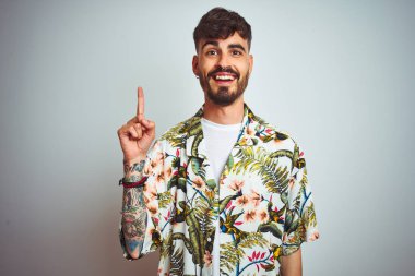 Tatilde dövmeli adam yaz lık gömlek giyerek izole beyaz arka plan üzerinde duran başarılı bir fikir ile parmak işaret. Çıktı ve mutlu. Bir numara.