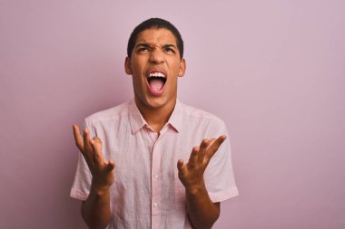 Yalnız pembe arka planda dikilen rahat gömlekli genç, yakışıklı bir Arap çılgın ve sinirli bir şekilde bağırıyor ve agresif bir ifadeyle kollarını kaldırıyor. Hayal kırıklığı konsepti.