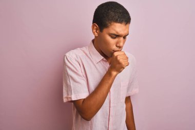 İzole edilmiş pembe arka planda dikilen rahat gömlekli genç yakışıklı Arap adam kendini kötü hissediyor ve soğuk algınlığı veya bronşitin belirtisi olarak öksürüyor. Sağlık hizmetleri kavramı.