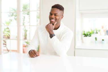 Afro-Amerikan yakışıklı beyaz masada emin çapraz kollar ve çeneme kaldırdı el ile gülümseme ile kameraya bakıyor. Pozitif düşünce.