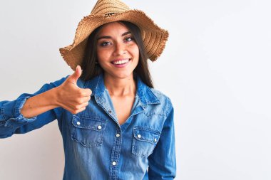 İzole edilmiş beyaz arka planda duran kot gömlekli ve şapkalı güzel bir kadın mutlu bir el hareketi yapıyor. Kameraya bakıp başarıyı gösteren ifade onaylanıyor.