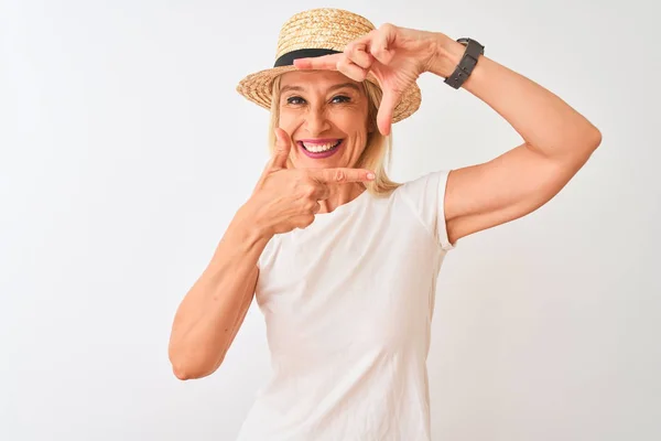 カジュアルなTシャツと帽子をかぶった中年女性が 幸せそうな顔で手と指でフレームを作る孤立した白い背景の上に立っている 創造性と写真のコンセプト — ストック写真
