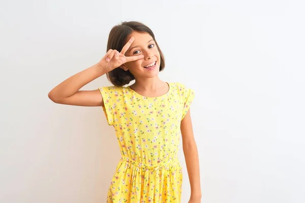 年轻美丽的女孩穿着黄色花卉礼服站在孤立的白色背景做和平符号用手指过脸 微笑欢快显示胜利 — 图库照片