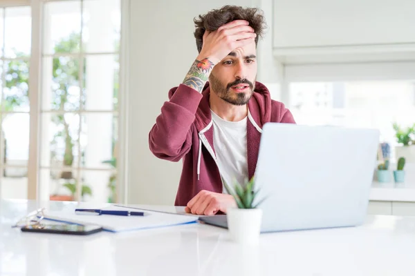 Young student man using computer laptop and notebook stressed with hand on head, shocked with shame and surprise face, angry and frustrated. Fear and upset for mistake.