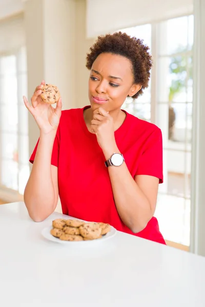 Unga Afroamerikanska Kvinna Äta Choklad Chips Cookies Allvarligt Ansikte Funderar — Stockfoto