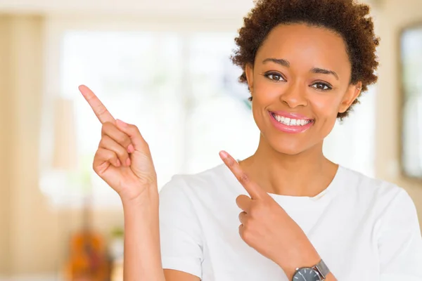 Young beautiful african american woman wearing casual white t-shirt smiling and looking at the camera pointing with two hands and fingers to the side.