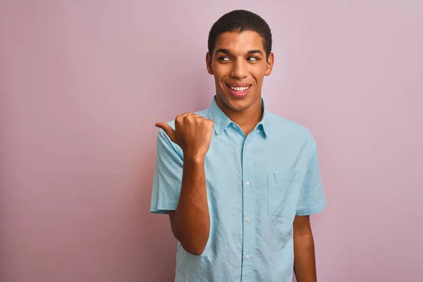 年轻英俊的阿拉伯男子 身穿蓝色衬衫 站在孤立的粉色背景上 面带微笑 面带微笑 大拇指指向旁边 — 图库照片