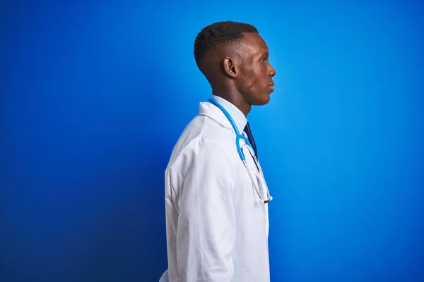 African american doctor man wearing stethoscope standing over isolated blue background looking to side, relax profile pose with natural face with confident smile.